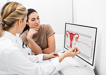 A gynecologist communicates with her patient, indicating the menstrual cycle on the monitor.