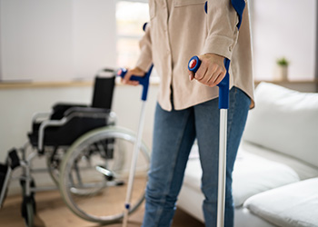 A woman using crutches with a wheelchair in the background