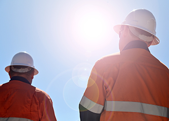 Two workers in hard hats outside in bright sunshine