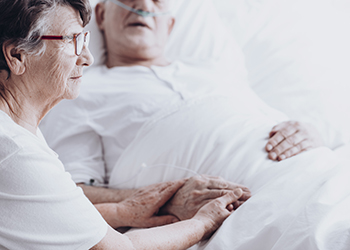 An older woman holds hand with her bedridden partner