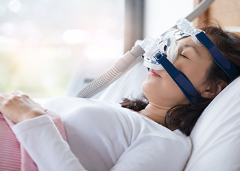 A woman using cpap machine to stop choking and snoring from obstructive sleep apnea with bokeh and morning light background