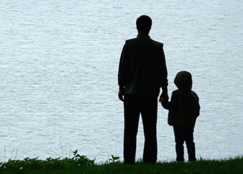 A father and son stand looking out at a lake