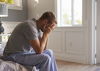 A man sits on a bed with his head in his hands