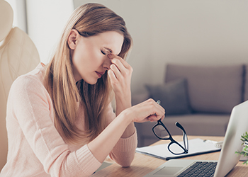 A women sits at a desk in pain with a headache