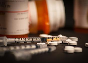 An injectable drug is loaded into a syringe while prescription medication is strewn about haphazardly.