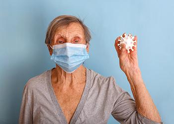 A female senior wearing a mask holds a model of a covid virus molecule in her hand
