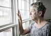 A lonely older woman looks out of her window