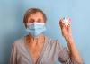 A female senior wearing a mask holds a model of a covid virus molecule in her hand