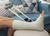 A person with a broken ankle in a plaster cast rests on a couch with crutches in the background 