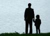 A father and son stand looking out at a lake